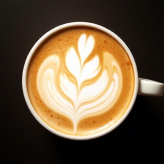 Latte art som former en sky på en mørk bakgrunn, fremhever baristaens ferdigheter.